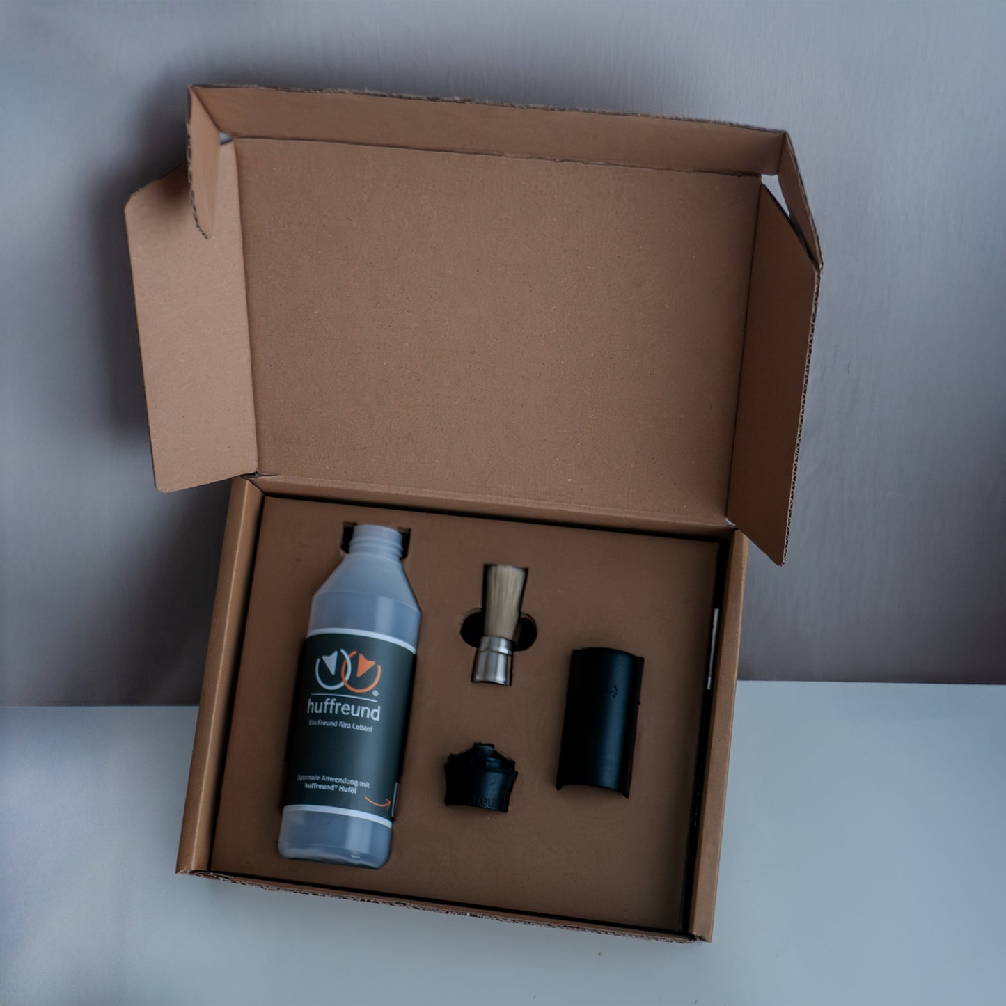 Der Huffreund Pro für Huföl auf Pferdehufen in seiner Produktverpackung bei Auslieferung zu Präsentationszwecken vor schlichtem Hintergrund.