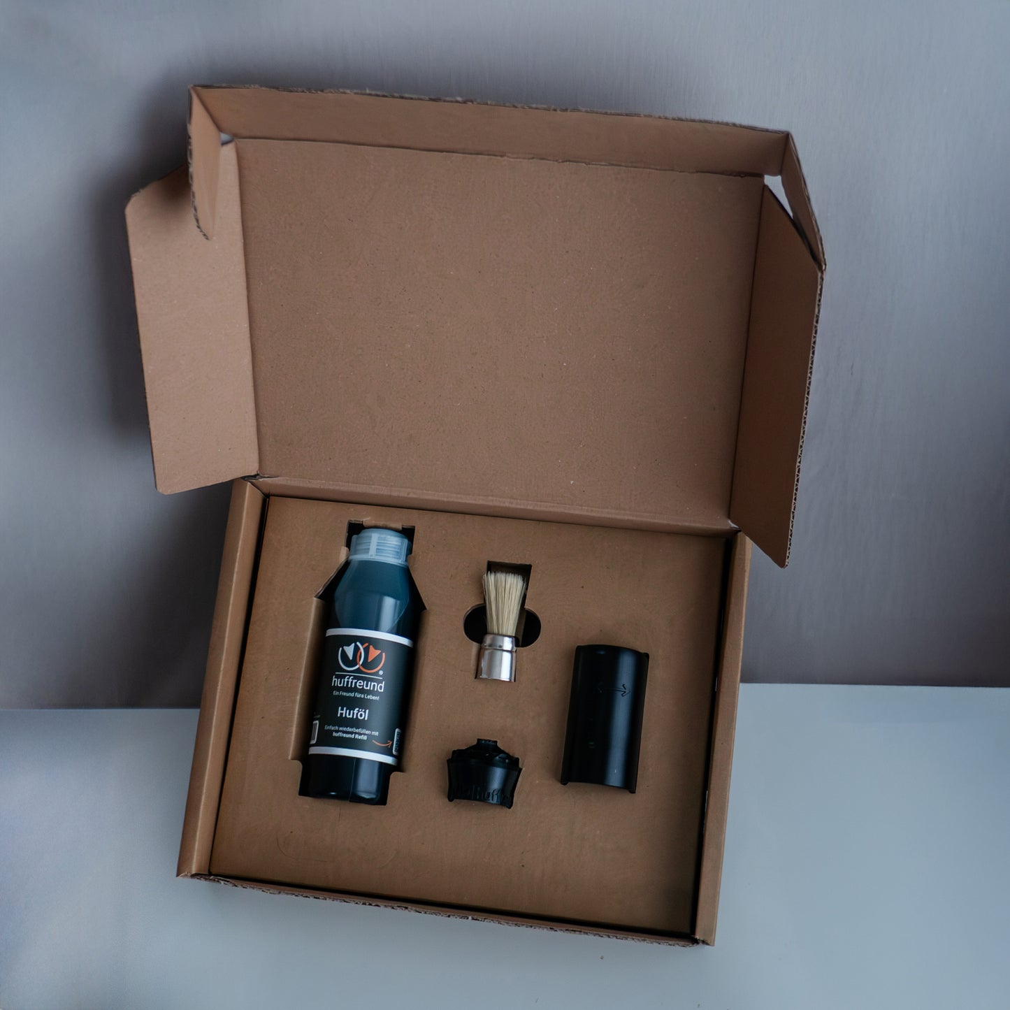 Der Huffreund Compact+ inkl. Huföl für Pferdehufe in seiner Produktverpackung bei Auslieferung zu Präsentationszwecken vor schlichtem Hintergrund. 