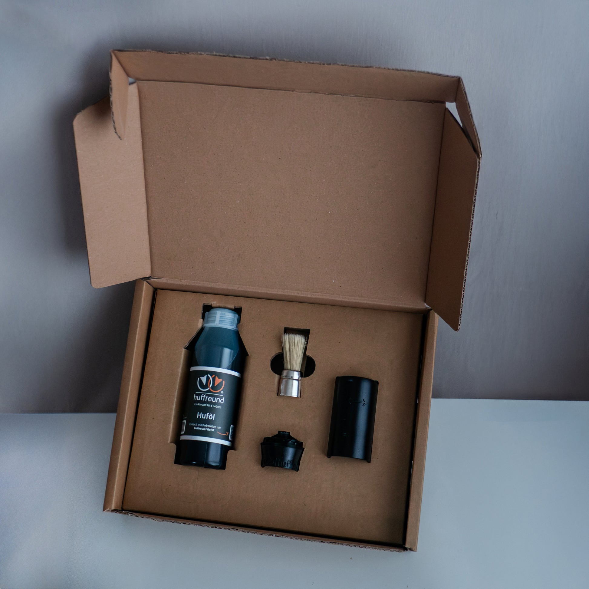 Der Huffreund Compact+ inkl. Huföl für Pferdehufe in seiner Produktverpackung bei Auslieferung zu Präsentationszwecken vor schlichtem Hintergrund. 