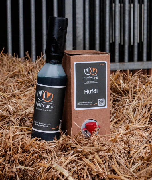 Huffreund Pro und Refill-Huföl auf Stroh vor Stallungen im Hintergrund nebeneinander stehend. 